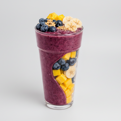 Layered smoothie with fruits and granola in a glass on a white background