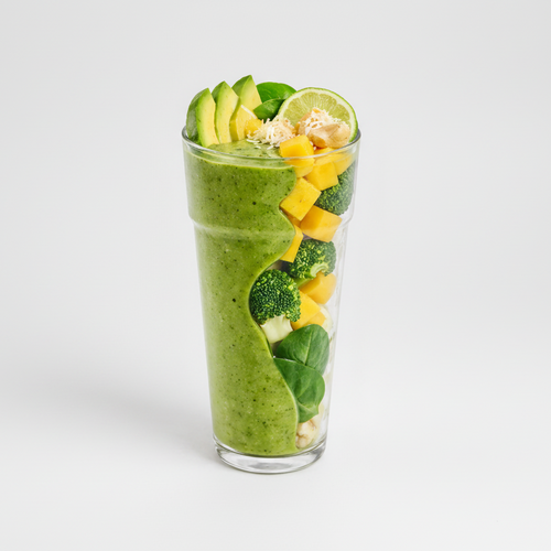 Green smoothie in a glass with mango, broccoli, and lime on a light gray background